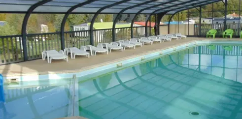 Piscine couverte avec chaises longues blanches et une chaise verte, Camping le Beauchêne