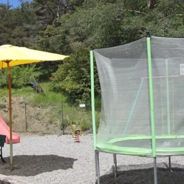 Piscine enfant avec parasol jaune et trampoline vert au Camping Le Champ Long