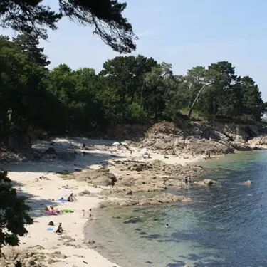 Plage de Camping Kerscolper avec sable, rochers et eau turquoise sous un ciel bleu.