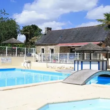 Piscine entourée d'une maison traditionnelle et d'ombrelles au Camping Kerscolper
