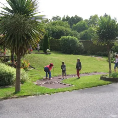 Enfants jouant au mini-golf dans un parcours en herbe, entourés de palmiers et de fleurs.