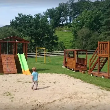 Enfant jouant près d'une aire de jeux en bois avec toboggan et train miniature, Camping Les Trois Sources.