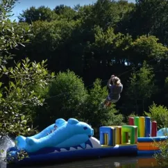 Enfant en équilibre sur un pont de zip au-dessus d'un lac avec une structure gonflable dauphin, Camping Les Trois Sources.