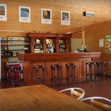 Bar en bois avec tabourets, frigo et affiches du Lot au Camping Les Trois Sources