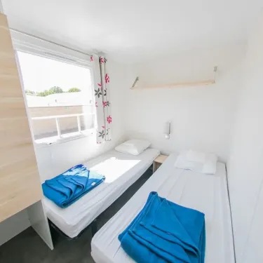 Chambre du Mobil Home Confort+ 3 Chambres 6 Personnes - La Ferme avec deux lits et draps bleus