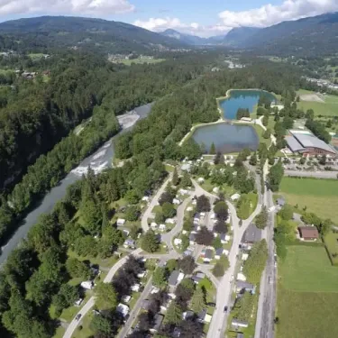Vue aérienne du Camping de Samoëns avec ses caravanes, lac et rivière verdoyante.