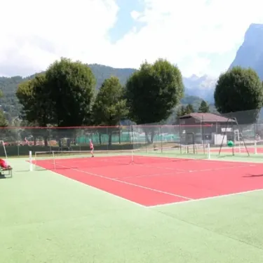 Camping de Samoëns : court de tennis rouge entouré d'arbres et de montagnes au loin.