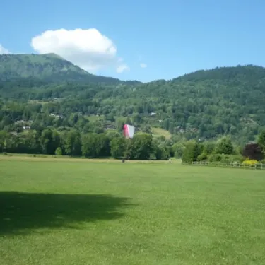 Camping de Samoëns : pelouse verte avec montagnes en arrière-plan et parapente en vol.