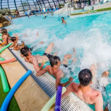 Enfants et adultes dans une piscine intérieure avec toboggan et eaux mouvementées au Camping Emeraude