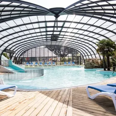 Piscine couverte avec toboggan et chaises longues au Camping Emeraude