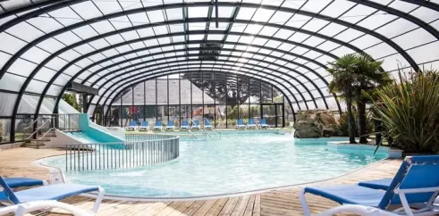 Piscine couverte avec toboggan et chaises longues au Camping Emeraude