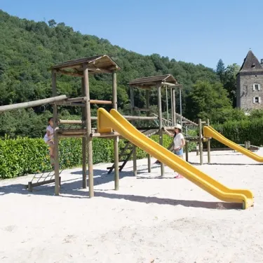 Piste de jeux en bois avec toboggans jaunes et château en arrière-plan au Camping Le Gibanel