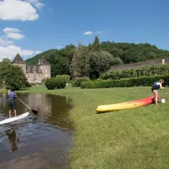 Camping Le Gibanel : personne sur paddleboard, kayak jaune à l'herbe près d'un château.