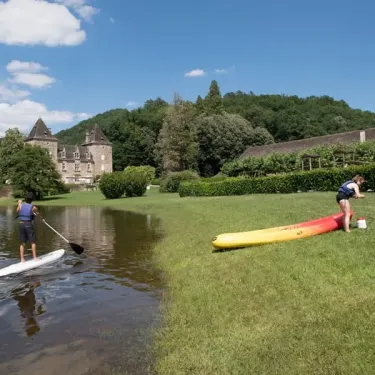 Camping Le Gibanel : personne sur paddleboard, kayak jaune à l'herbe près d'un château.