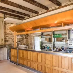 Bar en pierre avec comptoir en bois, éclairé par un lustre, dans le Camping Le Gibanel.