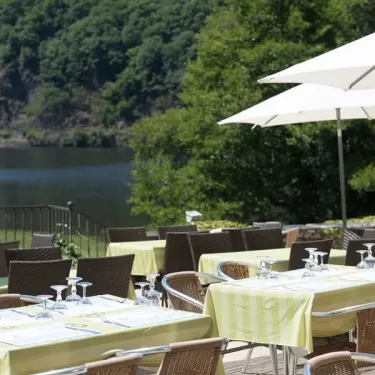 Terrasse de restaurant avec tables, chaises et parasols blancs au bord d'un lac au Camping Le Gibanel
