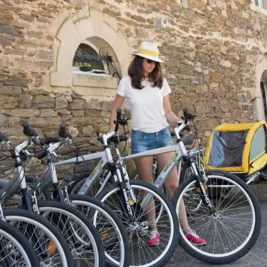 Femme avec casquette près d'une rangée de vélos et d'un chariot pour enfants au Camping Le Gibanel.