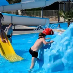 Enfants jouent dans la piscine avec une chute d'eau et un iceberg en plastique au Camping Du Domaine de L'Auzance.