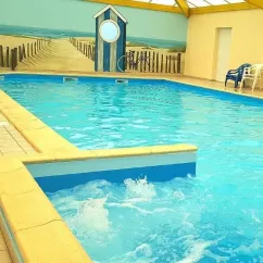 Piscine intérieure avec mur décoratif plage et chaises longues autour, au Camping Du Domaine de L'Auzance.
