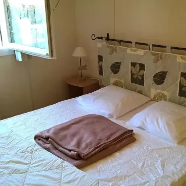 Lit double avec couverture pliée, lampe et tête de lit décorée - Chalet Grand Confort - Domaine de L'Auzance